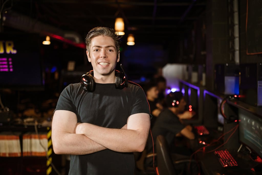 Smiling gamer standing with headphones in an illuminated gaming arena.